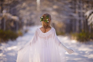 Beautiful girl in a white dress walks in the winter forest. Bride on a background of a winter...