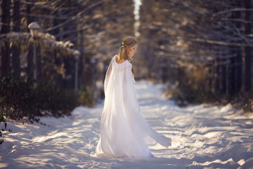 Beautiful girl in a white dress walks in the winter forest. Bride on a background of a winter...