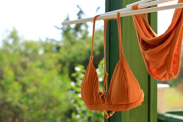 Bright orange bikini swimsuit hanging air drying on clothing line on balcony. Summer concept of...