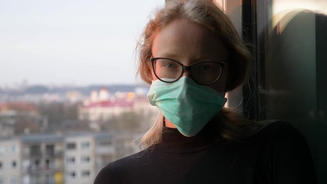 worried young woman with half face in shadow with medical mask looks to a camera as illustration of corona virus epidemic danger