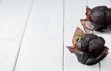Two homemade chocolate muffin, decorated leaf mint on a white wooden table. Close up, copy space