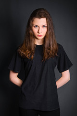 Beautiful, young girl with long hair, in black clothes, posing in studio on a gray background. A model with clean skin.