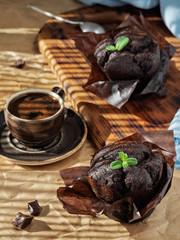 Muffins with chocolate decorated with a leaf of mint arranged on a gray paper background, close-up. Natural sunlight. Nearby is a cup of espresso and pieces of chocolate. Shallow focus