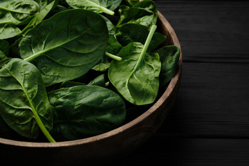 wooden plate with fresh spinach leaves on black background. closeup