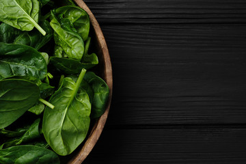 wooden plate with fresh spinach leaves on black background. closeup