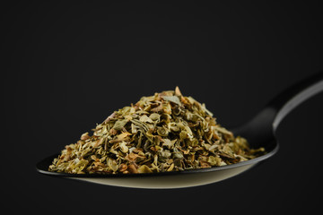 black spoon with Italian seasoning - dried oregano with thyme, basil and vegetables. black...