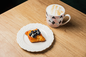 Danish pastry with custard and bog bilberry on a white plate and a mug of flat white coffee