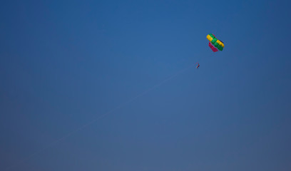 Fototapeta na wymiar multicolored parachute on a cable with passengers flying through the blue sky
