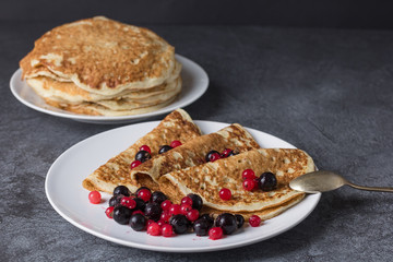 Homemade pancakes with black and carcourined currant berries on a plate against a dark background