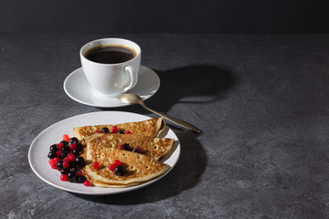 A cup of coffee and pancakes with berries on a teel. Delicious breakfast.