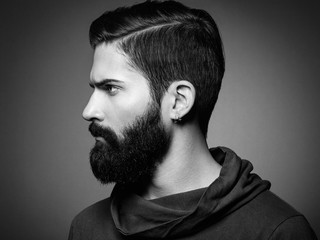 Portrait of handsome man with beard and mustache. Close-up image of serious brutal bearded man on dark background. Black and white photography - obrazy, fototapety, plakaty