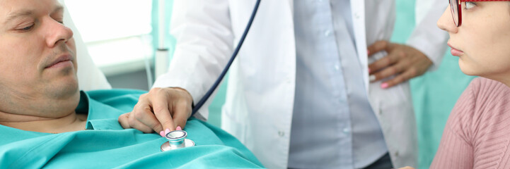 Close-up of beautiful physician listening to action of unhealthy patient heartbeat or breathing. Upset wife and husband waiting for decision. Treatment and healthcare concept