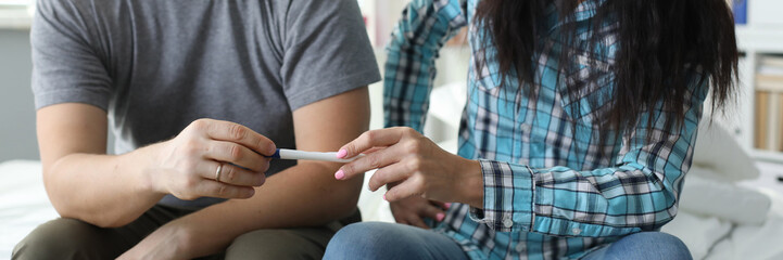 Portrait of expectant mother passing positive pregnancy test to husband. Happy boyfriend and girlfriend ready to become parents. Wife with smile on face sitting on bed