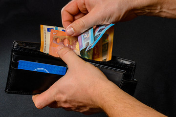 Man hand pulling money from wallet, black background and black wallet.