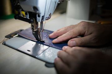 A man sews from leather on a sewing machine. Hands and sewing. Production of leather goods using a sewing machine