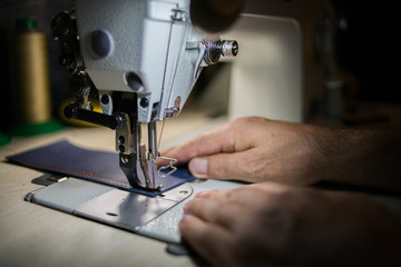 A man sews from leather on a sewing machine. Hands and sewing. Production of leather goods using a sewing machine