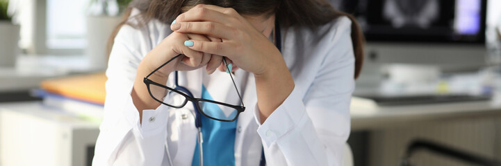 Portrait of sad discouraged specialist in white medical gown at clinic. Physician sitting head down at table in cabinet. Medicine and healthcare concept