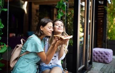 Portrait of two young women eating pizza outdoors, having fun together.