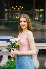 A beautiful young Caucasian girl holding a bouquet of roses and standing near the balusters in the city and smiling