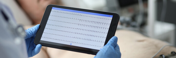 Focus on hands of female doctor examining condition of patient illness heart and touching screen of modern tablet with cardiogram. Medicine and healthcare concept