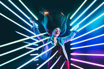 Attractive dancing girl, hair flying, neon light. Full-length portrait of girl posing with hands up.