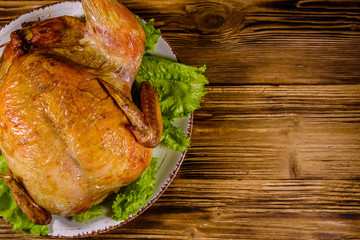 Plate with roasted whole chicken and lettuce leaves on a wooden table. Top view