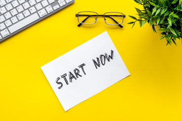 Start now. Motivative text on yellow office desk top-down