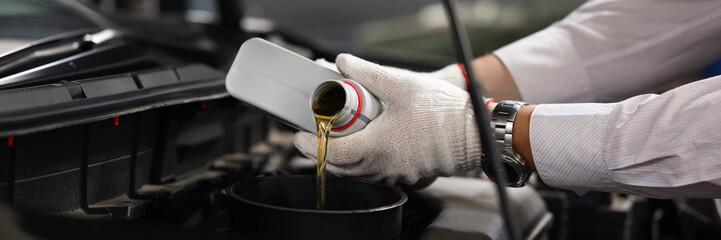 Focus on male specialist hands holding canister of machinery liquid and pouring under hood of sportcar with precise accuracy. Automotive checkup concept