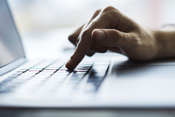 Male hands typing on laptop keyboard in sunny office, business and technology concept. Close up