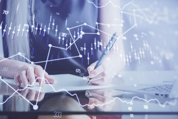 A woman hands writing information about stock market in notepad. Forex chart holograms in front. Concept of research.