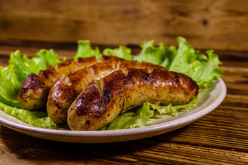 Plate with roasted sausages and lettuce leaves on a wooden table