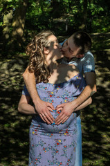 Young couple in love husband and pregnant wife kiss in the park, happy family
