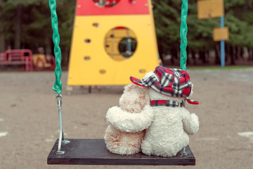 Two Teddy bears hugging each other sitting on a swing. The concept of love, relationships.