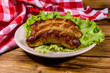 Plate with roasted sausages and lettuce leaves on a wooden table