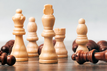 On the table are white chess pieces. The king’s figure is in focus in the center; the remaining figures are out of focus. Around them are black pieces. The concept of business, success, teamwork..