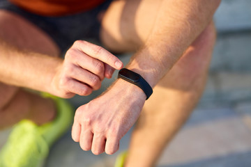 Young man using hand watch during exercising / stretching in urban park.
