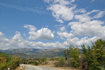 Fototapeta na wymiar The road goes into the distance among beautiful mountains. Beautiful white clouds on the horizon