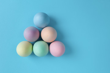 Colorful Easter eggs in triangle shape on blue background - top view with copy space