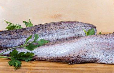Uncooked defreezed hake with fresh parsley on cutting board, fragment