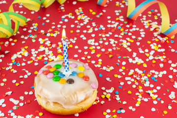 Delicious birthday cake with a burning candle, confetti and streamers, red background