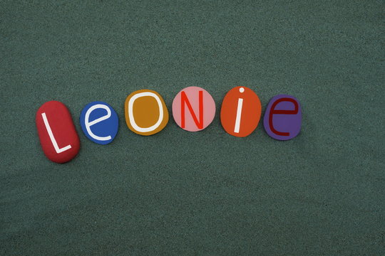 Leonie, female given name composed with colored stone letters over green sand