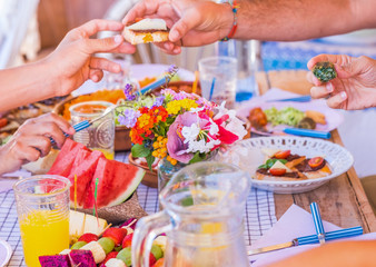 Group of hands sharing food and drink. Caucasian peoples enjoying brunch or meal together. Fruits and vegetables on the wooden table. Sunlight outdoor on the terrace