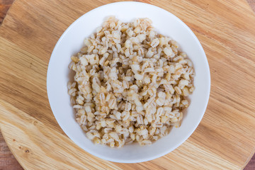 Pearl barley porridge in bowl on wooden surface, top view