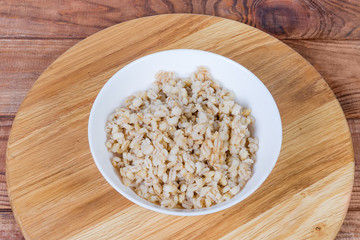 Pearl barley porridge in bowl on wooden surface