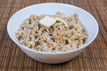 Pearl barley porridge with butter in white bowl close-up