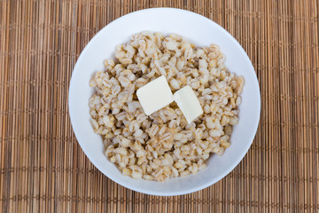 Pearl barley porridge with butter in white bowl, top view