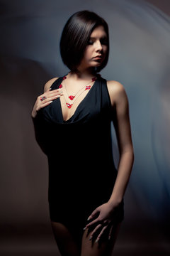 Monochrome portrait of the riddler beautiful slender girl in a black dress on a black background in the studio. Concept of femininity and beauty and grooming. Place for advertising