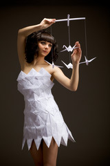 Pensive young girl in an origami dress holds an origami bird in his hands. Puppets on a black...