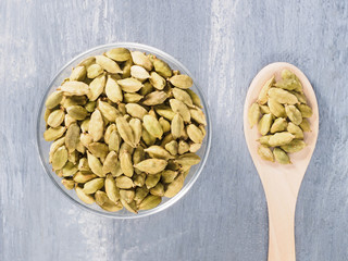Spice green cardamom (Elettaria cardamomum) in transparent bowl and wooden spoon on gray concrete background closeup. The proper nutrition concept