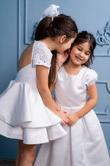 Fototapeta na wymiar Two whispering kids in white dresses, on a gray background.